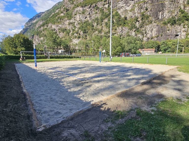 Vista del campo da beach volley di Osogna con sabbia dorata e una montagna pittoresca sullo sfondo, prenota il tuo gioco oggi!
